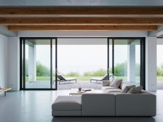 Contemporary living room with exposed concrete and raw wood, floor-to-ceiling glass doors opening to an outdoor patio with soft natural daylight.