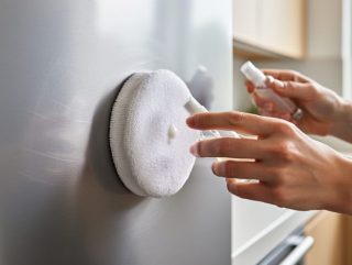 Hands polishing a lightly scratched stainless steel kitchen appliance with a microfiber pad and polishing compound bottle.